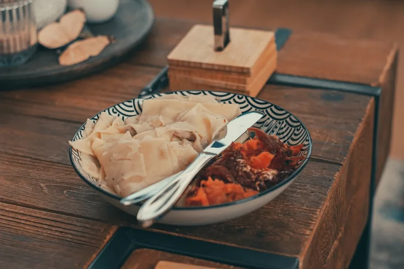 Un cuenco de cerámica rústica lleno de fideos y verduras guisadas sobre una mesa de madera, con palillos y una pequeña caja de madera al lado, luz natural suave, una comida estacional tranquila