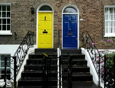 A bright red front door of a modern home with potted plants on either side and a clear, uncluttered pathway leading to it