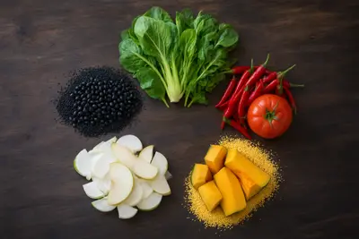 Cinco ingredientes sobre madera oscura: frijoles negros, bok choy, chiles rojos y tomate, manzana en rodajas y calabaza con mijo amarillo