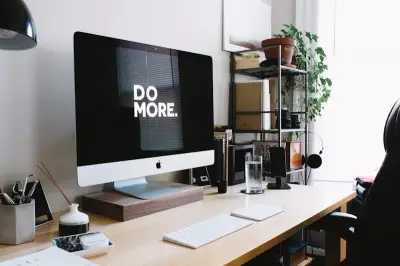 A clean wooden desk facing the room entrance, with a solid wall behind it, a plant on the left, and natural light from a side window