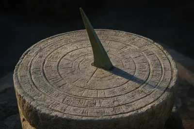 Un reloj de sol de piedra desgastada, con anillos concéntricos grabados y un gnomon de bronce en el centro, proyectando una sombra nítida sobre la esfera bajo una luz lateral cálida